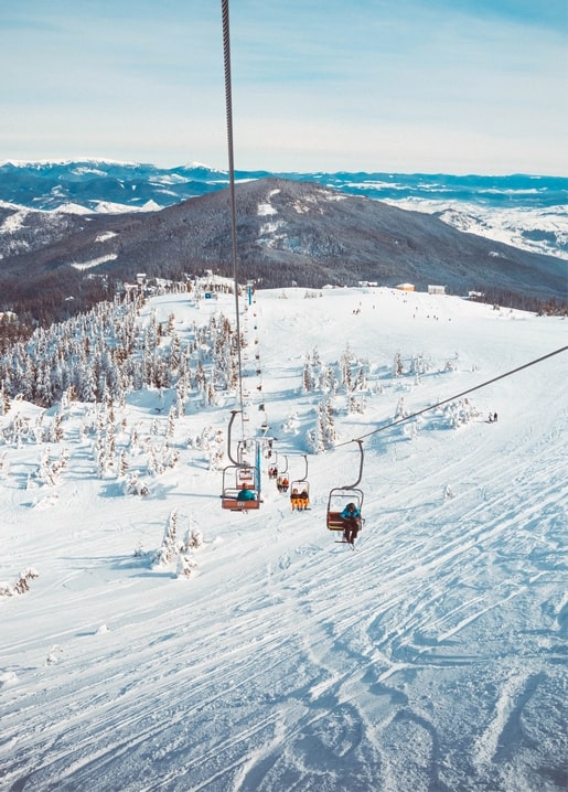 Sessellift mit Skifahrern über einem verschneiten Berghang mit Kiefernwald