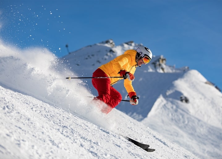 Skier in a yellow jacket carving through powder snow on a sunlit mountain slope
