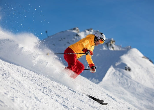 Skier in a yellow jacket carving through powder snow on a sunlit mountain slope
