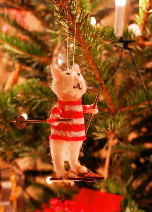 Felted wool cat ornament in a red-striped sweater skiing on a candlelit Christmas tree branch