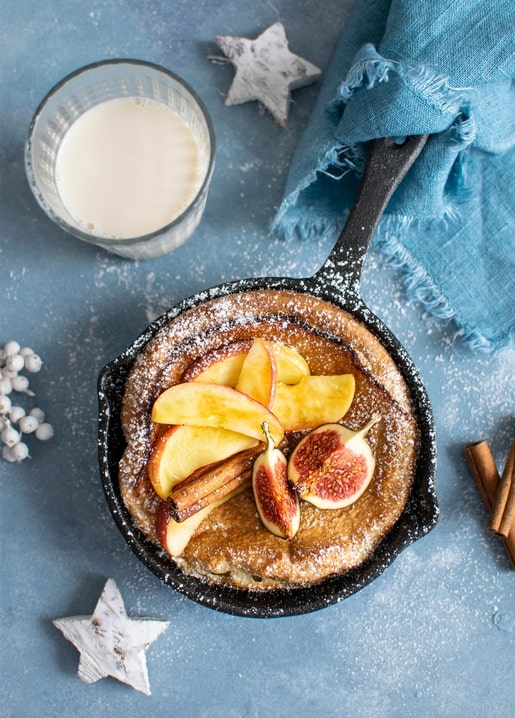 Skillet pancake topped with apple slices and fig, served with a glass of milk