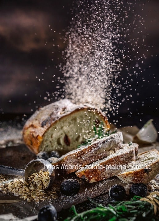 Dunkles aufgeschnittenes Brot mit fallendem Mehlstaub neben Oliven, Hafer und Knoblauch