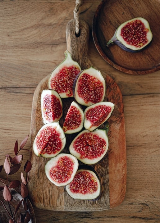 Sliced ripe figs with red flesh arranged on a wooden board beside a dried eucalyptus branch
