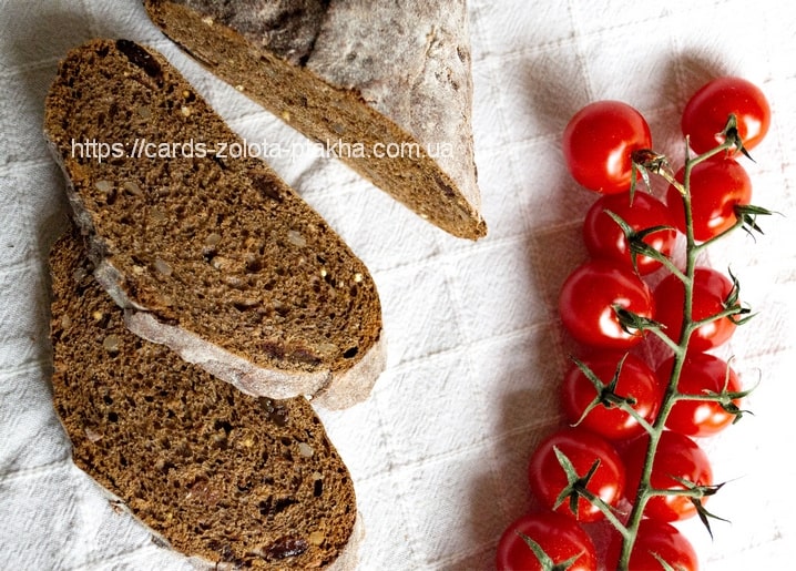 Geschnittenes Roggenbrot neben einer Rispe reifer Kirschtomaten am Zweig, von oben fotografiert.