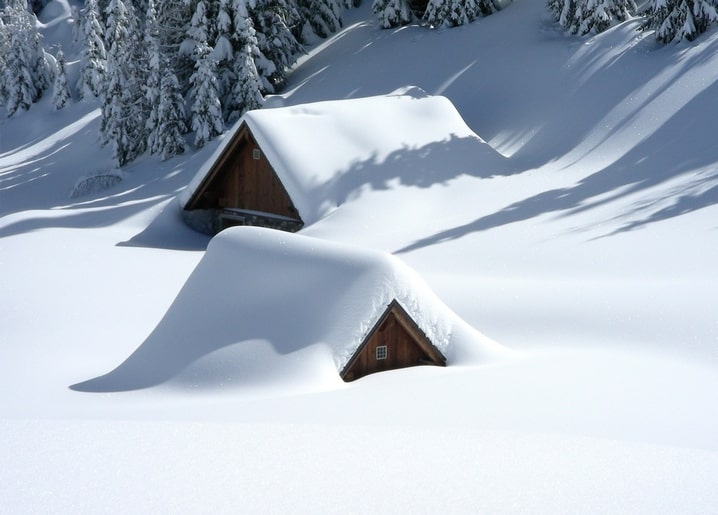 Two wooden cabins almost buried under deep snowdrifts in a quiet forest