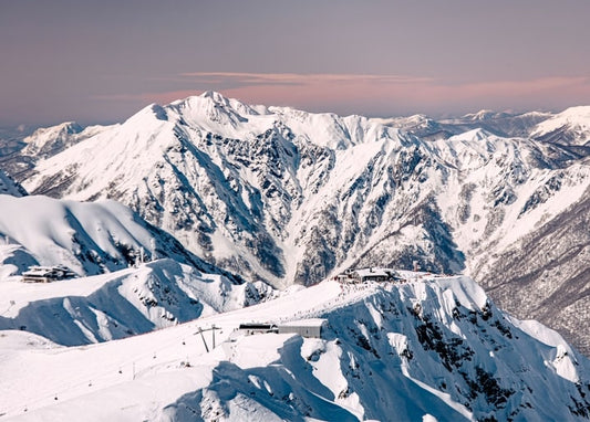 Aerial view of snow-capped mountain peaks at dusk with a small ski resort