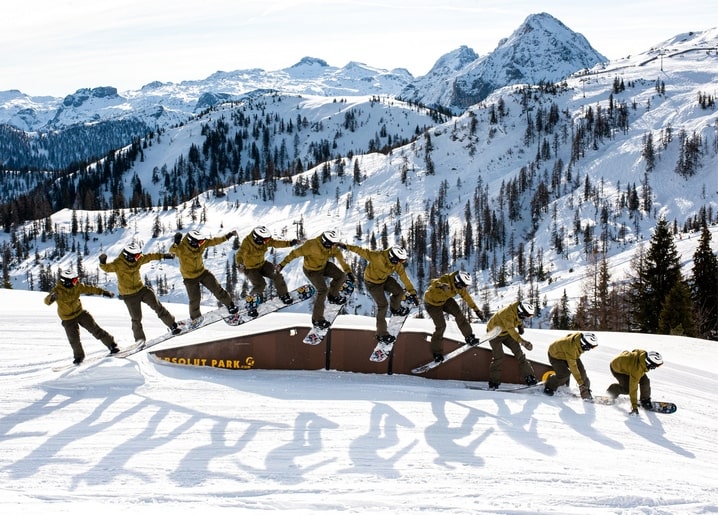 Multi-exposure sequence of a snowboarder jumping a rail in the mountains
