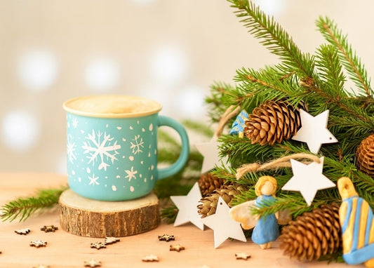 Türkisfarbene Tasse mit Schneeflocken-Muster neben Tannenzweigen und Holzsternen