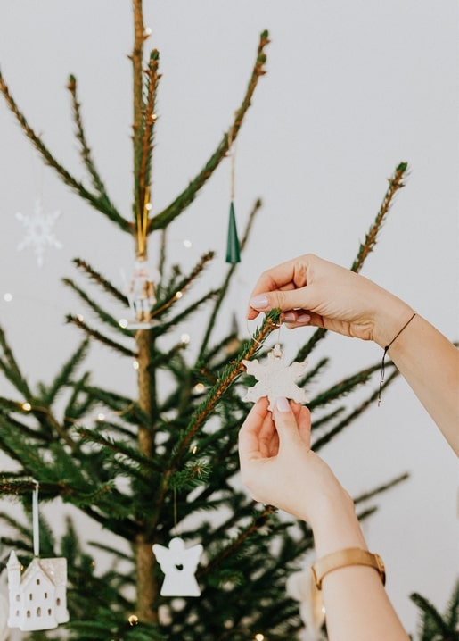 Руки вішають білу прикрасу-сніжинку на різдвяну ялинку з гірляндою