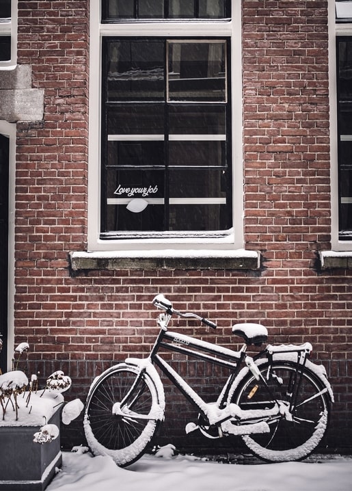 Schneebedecktes Fahrrad lehnt im Winter an einer Backsteinwand unter einem Fenster
