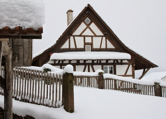 Snow-covered half-timbered house behind a frosted wooden picket fence