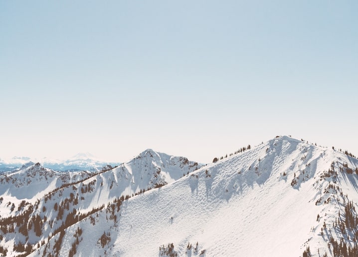 Schneebedeckter Gebirgskamm mit freiliegendem Gestein unter blassem, dunstigem Himmel