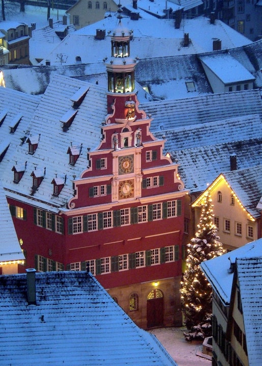 Luftaufnahme schneebedeckter Dächer um ein rotes Rathaus mit Staffelgiebel und Weihnachtsbaum