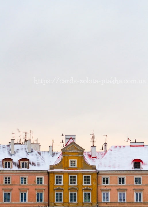 Schneebedeckte Dächer bunter ockerfarbener und rosa Altstadthäuser unter blassem Winterhimmel