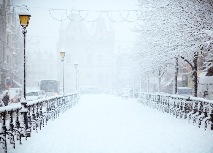 Snow-covered European street with old-style lanterns fading into fog.