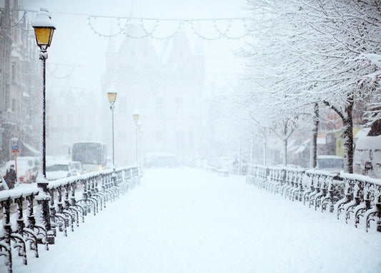 Snow-covered European street with old-style lanterns fading into fog.