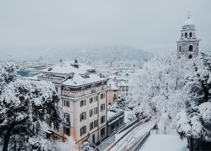 Aerial view of a snow-covered European town with a stone bell tower in fog