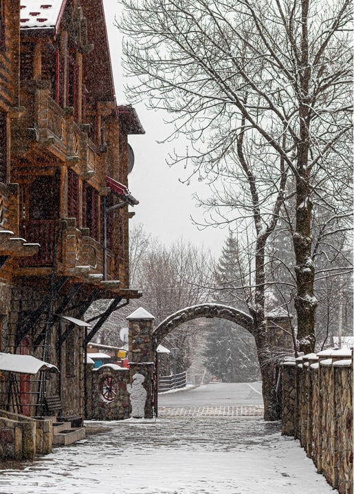 Verschneite Dorfstraße mit Holzchalets und Steinbogen