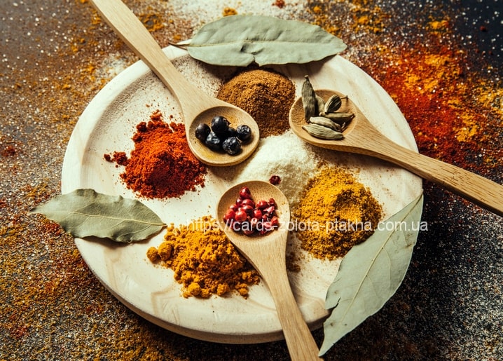 Wooden plate with spoons of paprika, cardamom, turmeric, and dried berries surrounded by bay leaves