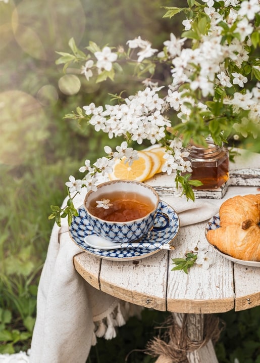 Чашка чаю, лимон, мед і круасани під гілкою білого цвіту