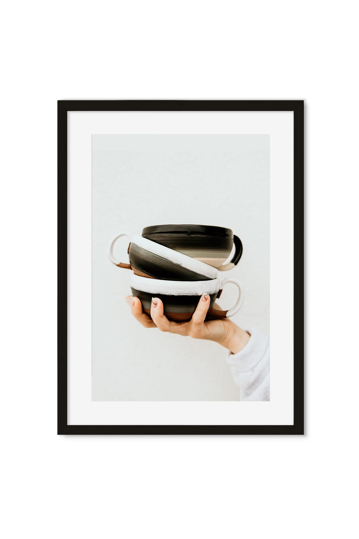 A hand holding a stack of glazed black-and-white ceramic bowls against a plain background