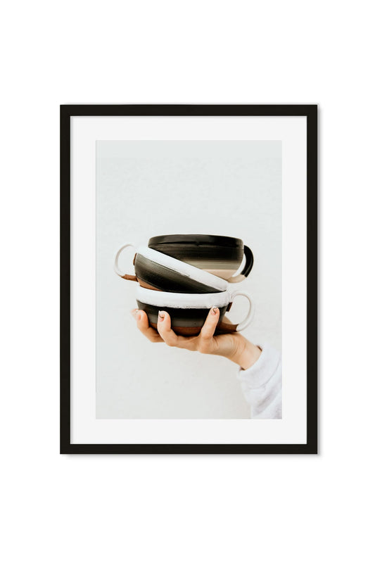 A hand holding a stack of glazed black-and-white ceramic bowls against a plain background
