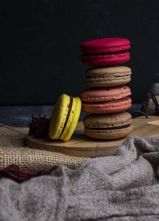 Vier gestapelte Macarons in Himbeere, Kaffee, Koralle und Zitrone auf Holz