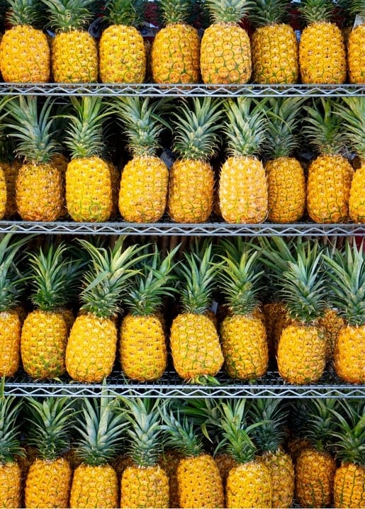 Reihen von Ananas mit stacheligen grünen Kronen auf Metallregalen eines Marktes