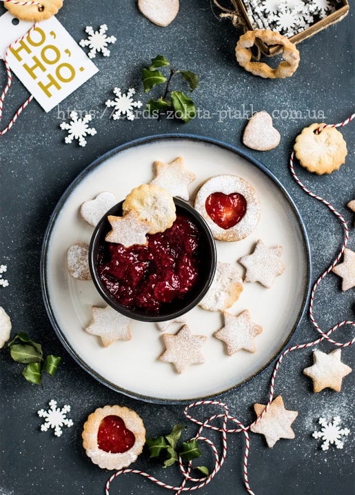 Stern- und Herzkekse mit Beerenmarmelade, Schneeflocken und ein „Ho Ho Ho“-Anhänger auf einem Teller