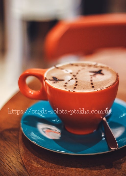 Orange cup of latte with a star traced in the foam, on a teal saucer