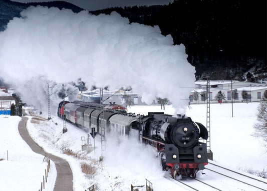 Black steam locomotive pulling carriages through a snowy mountain valley with billowing smoke