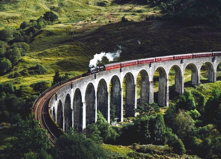 Red steam train crossing the arched Glenfinnan Viaduct in the Scottish Highlands