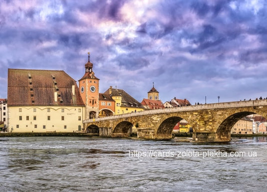 Steinerne Bogenbrücke zur Regensburger Altstadt mit Uhrturm und steilem Dach unter Abendwolken.