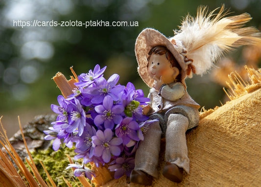 Strohhut-Figur eines Jungen neben einem Strauß violetter Leberblümchen