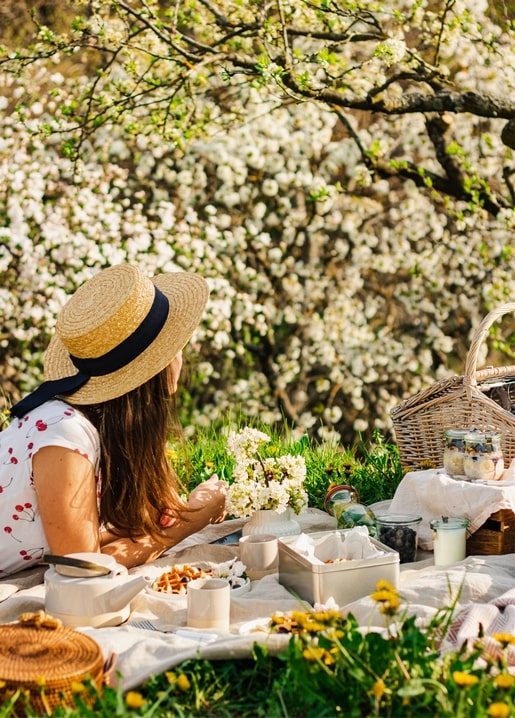 Frau im Strohhut beim Picknick unter blühenden Bäumen