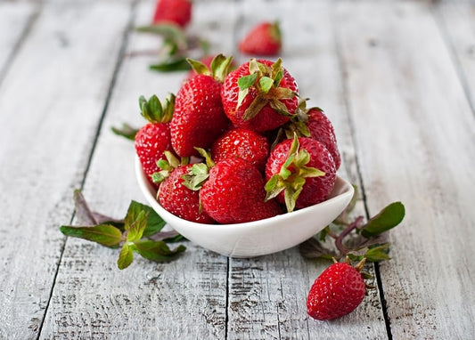 Weiße Schale mit reifen Erdbeeren und Minzzweigen auf Holztisch