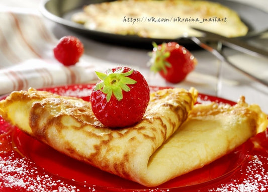 Gefalteter Crêpe mit Erdbeere auf rotem Teller, im Hintergrund ein Crêpe in der Pfanne