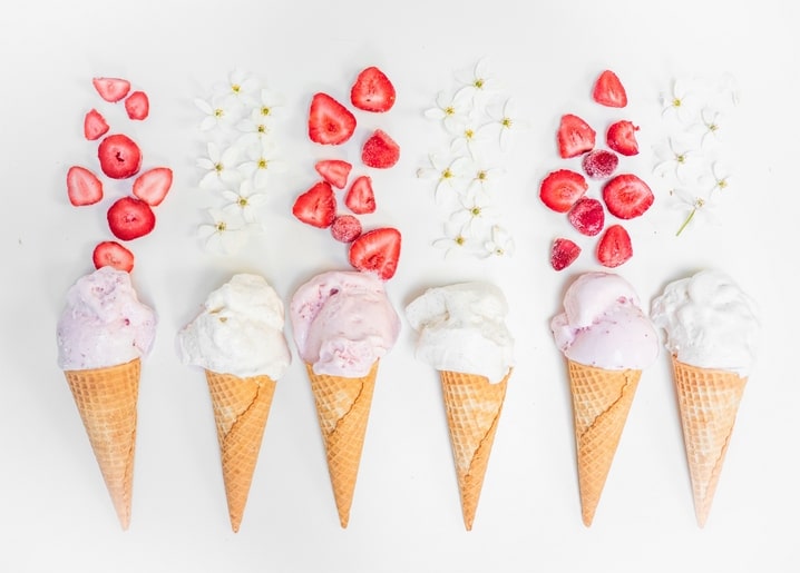 Six strawberry ice cream cones with fresh berries and white spring blossoms on a white background