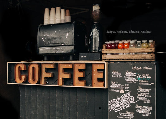 Hölzernes „COFFEE“-Schild neben einer Espressomaschine und Flaschengetränken am Straßenstand