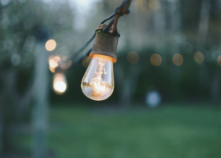 Leuchtende Lichterkette hängt abends im Garten vor unscharfem grünem Hintergrund.