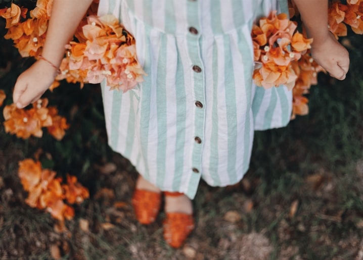 Gestreiftes Sommerkleid und rostrote Sandalen zwischen orangefarbenen Bougainvillea-Blüten