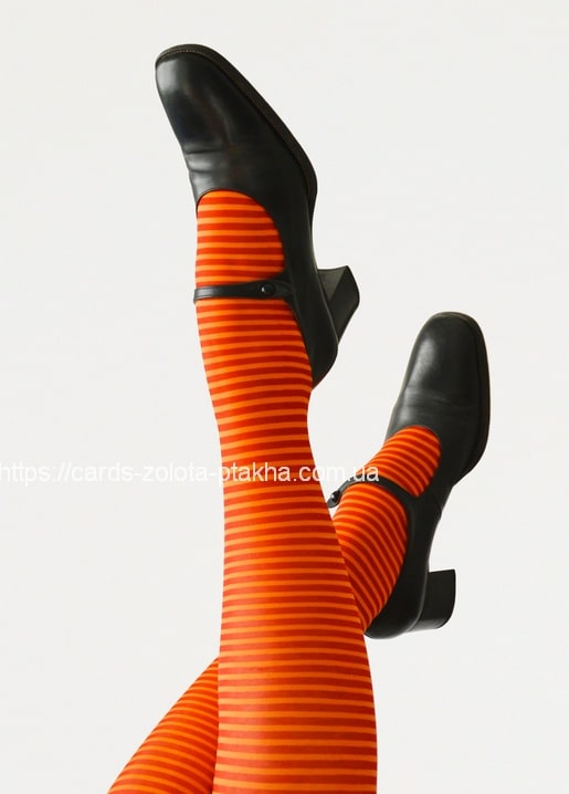 Beine in orange-rot gestreifter Strumpfhose und schwarzen Riemchenschuhen vor weißem Hintergrund.