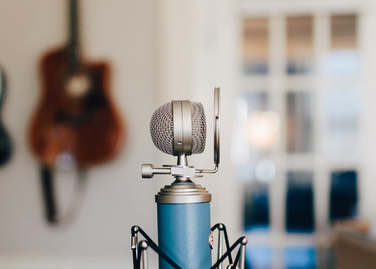 Blaues Studio-Kondensatormikrofon auf einem Stativ, im Hintergrund eine unscharfe Akustikgitarre