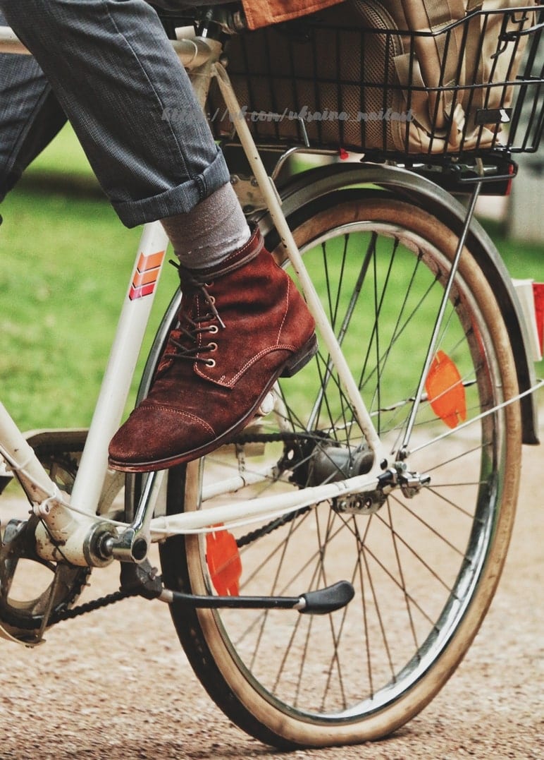Brauner Wildlederstiefel auf dem Pedal eines cremefarbenen Vintage-Fahrrads mit Korb
