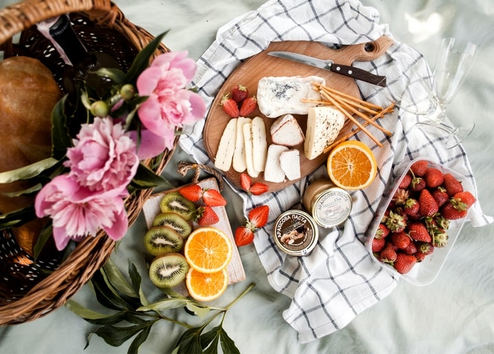 Picknick von oben mit Käse, Erdbeeren, Kiwi, Zitrusfrüchten, rosa Pfingstrosen und einem Weidenkorb