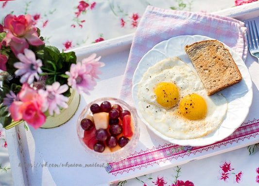 Breakfast tray with sunny-side-up eggs, toast, fruit and pink flowers