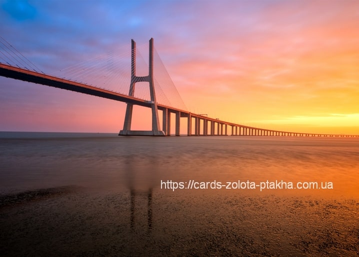 Schrägseilbrücke vor rosa-goldenem Sonnenuntergang, gespiegelt im nassen Sand