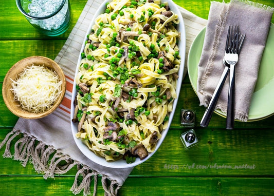 Oval platter of tagliatelle with mushrooms, peas and herbs beside grated parmesan