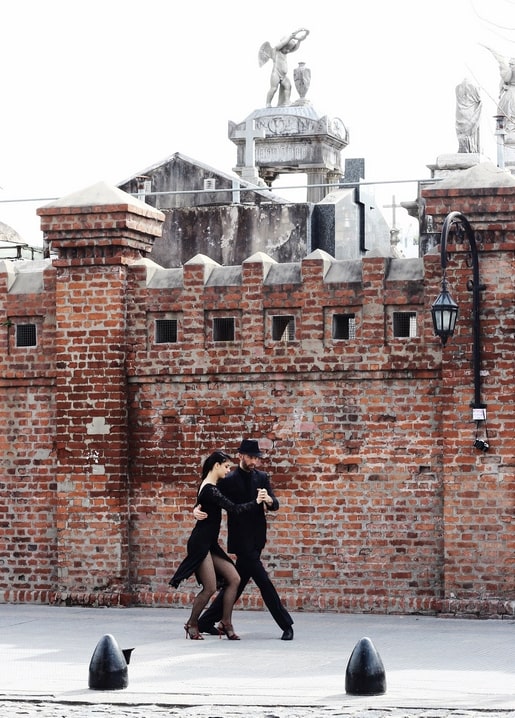 Paar tanzt Tango in Schwarz vor einer alten Backsteinmauer mit Statuen