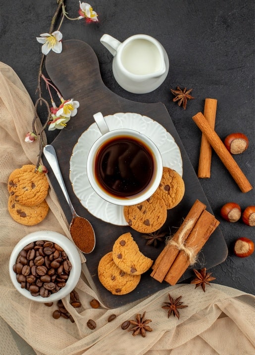 Чашка чаю з паличками кориці, печивом та кавовими зернами